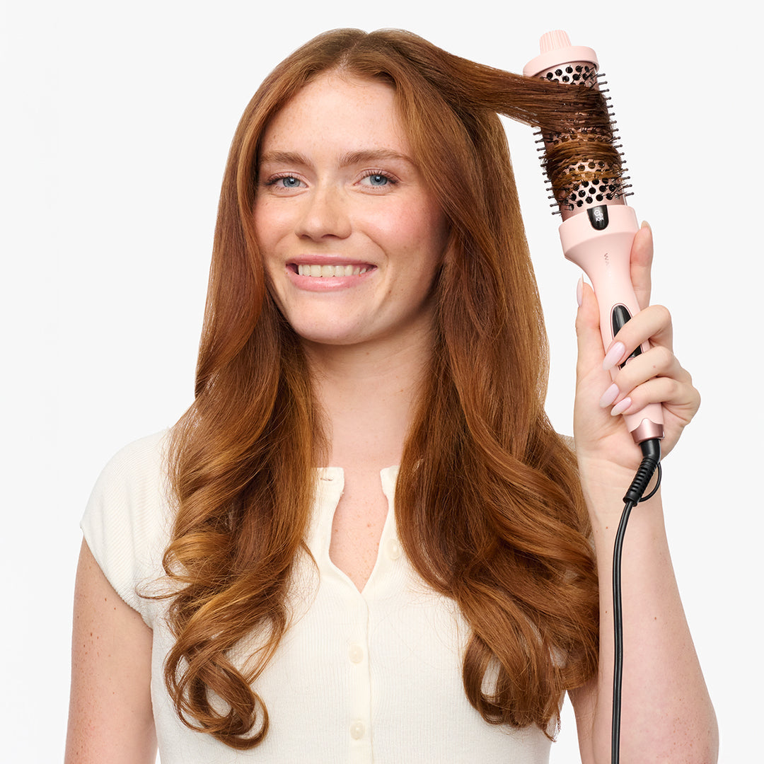Woman using a pink blowout boost on her hair against a white background