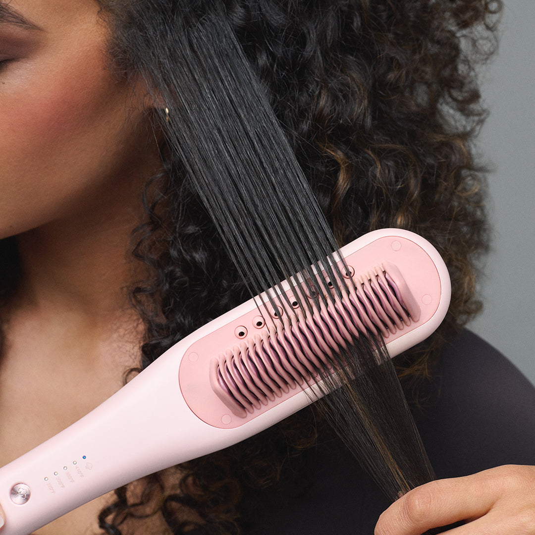 Person using a pink steamline pro on curly hair against a neutral background