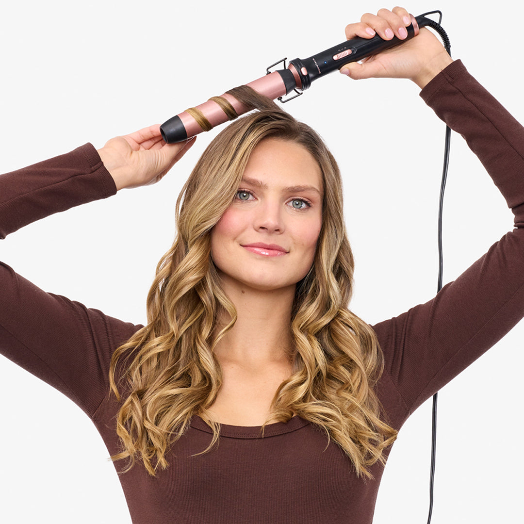 Woman getting her hair styled with a curling iron against a white background