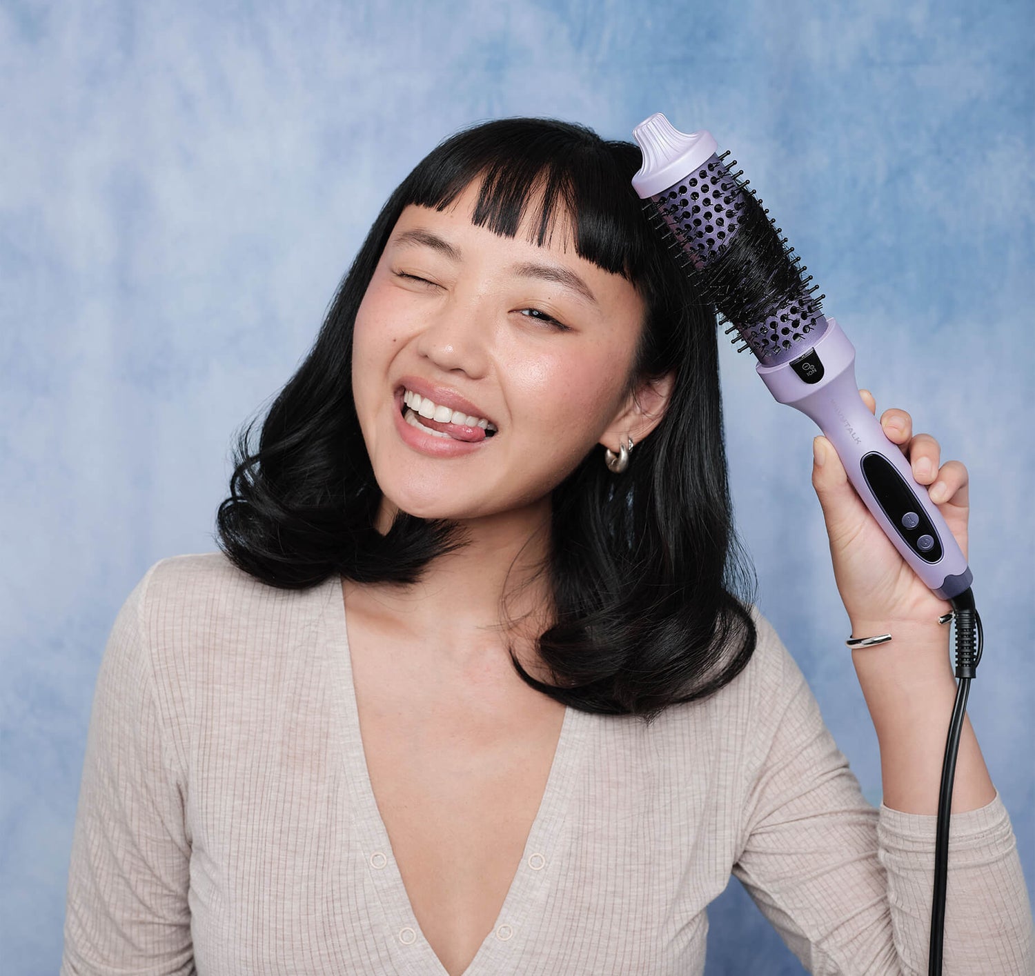 Woman holding a purple hair styling tool against a blue background