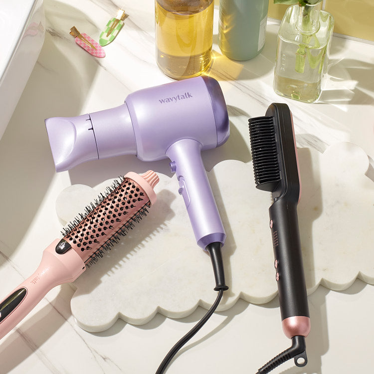 Purple hair dryer with round styling brush and black comb on white surface with beverages and decor in background