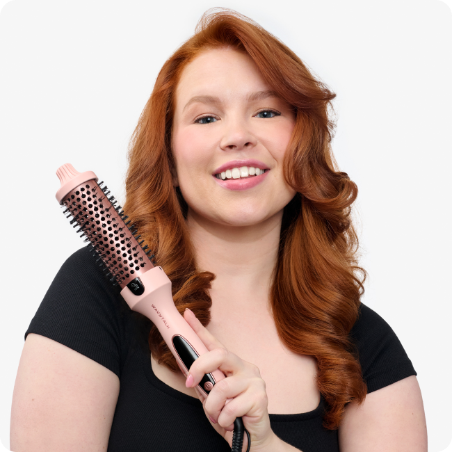 Woman with red hair holding a hair styling tool against a white background