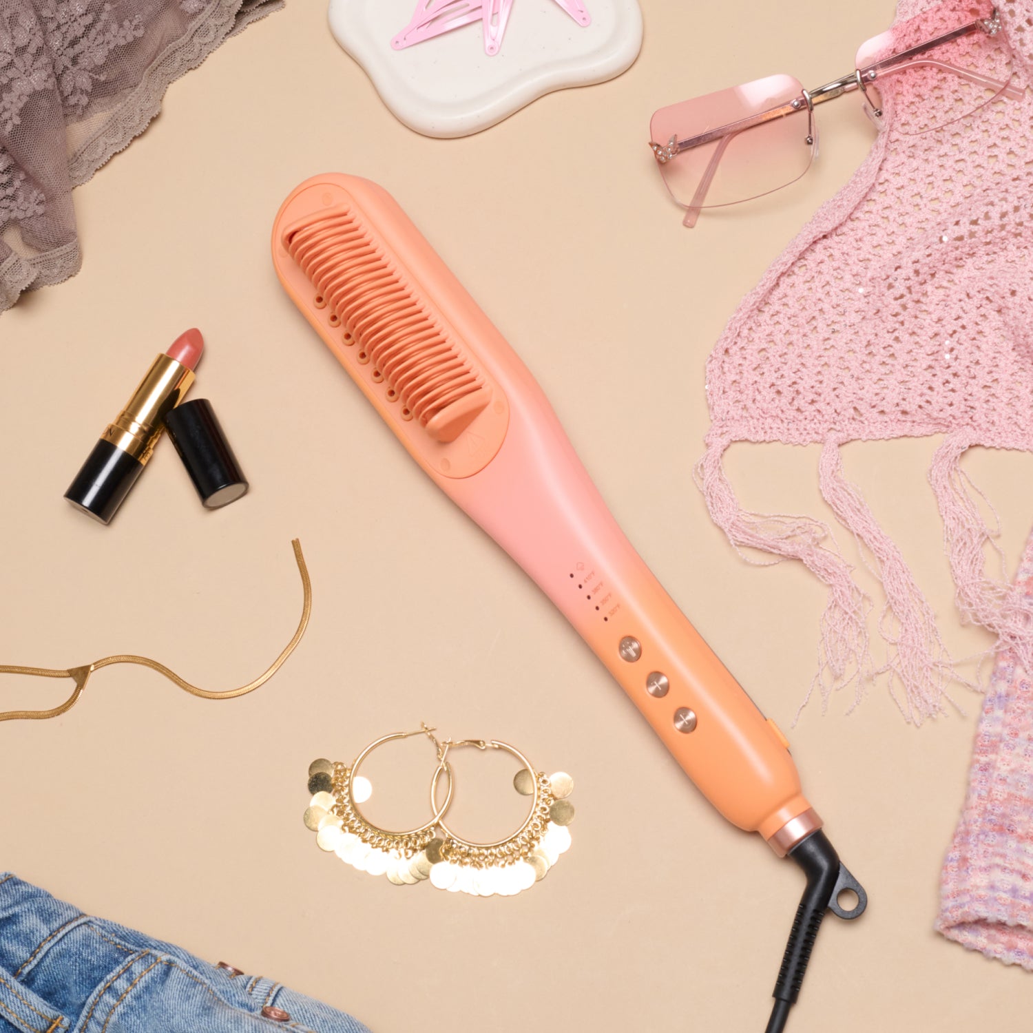 Orange hair straightener on a beige surface with lipsticks, glasses, and jewelry.