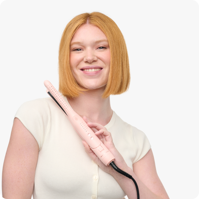 Woman holding a pink hair straightener against a white background