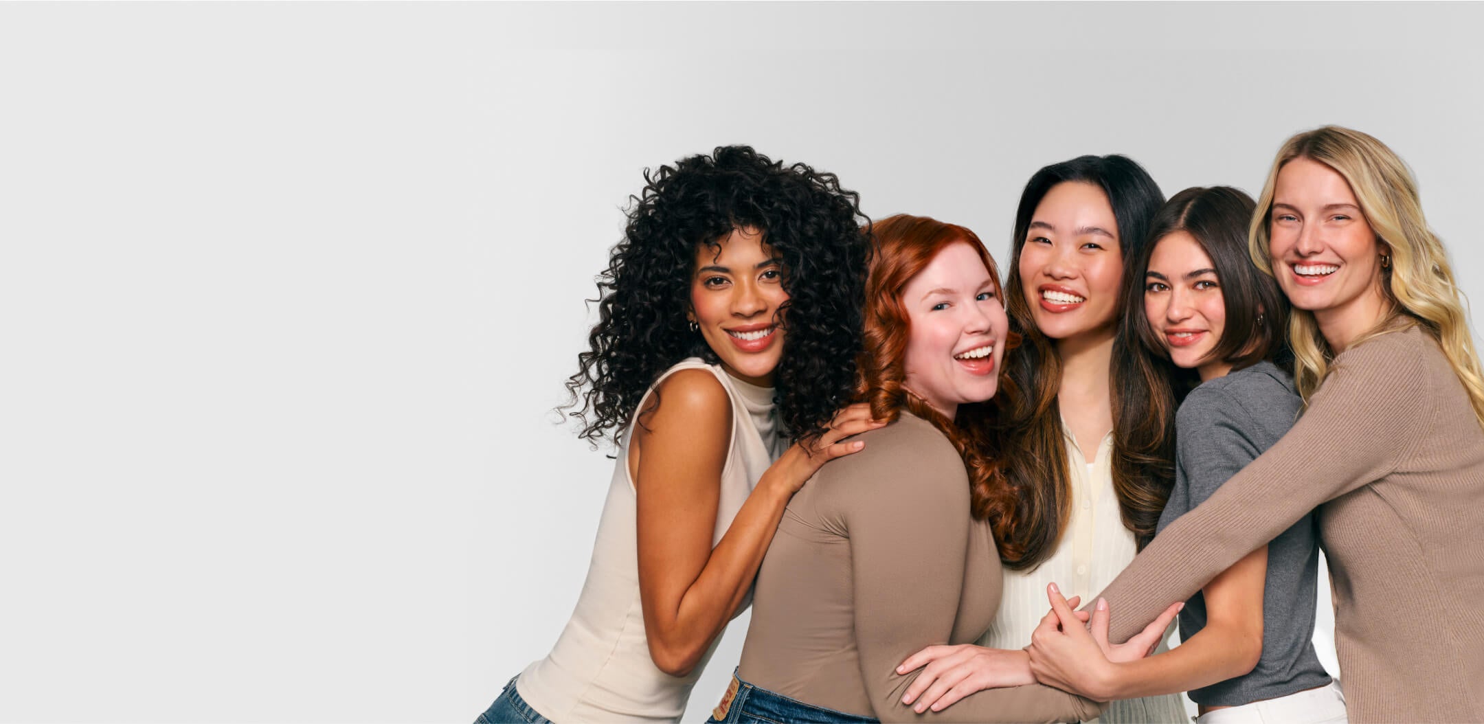 Group of five diverse, smiling women with different hair styles against a light gray background.