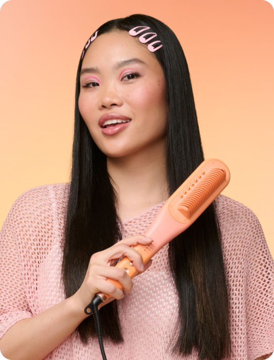 Woman using a hair straightener against a peach background