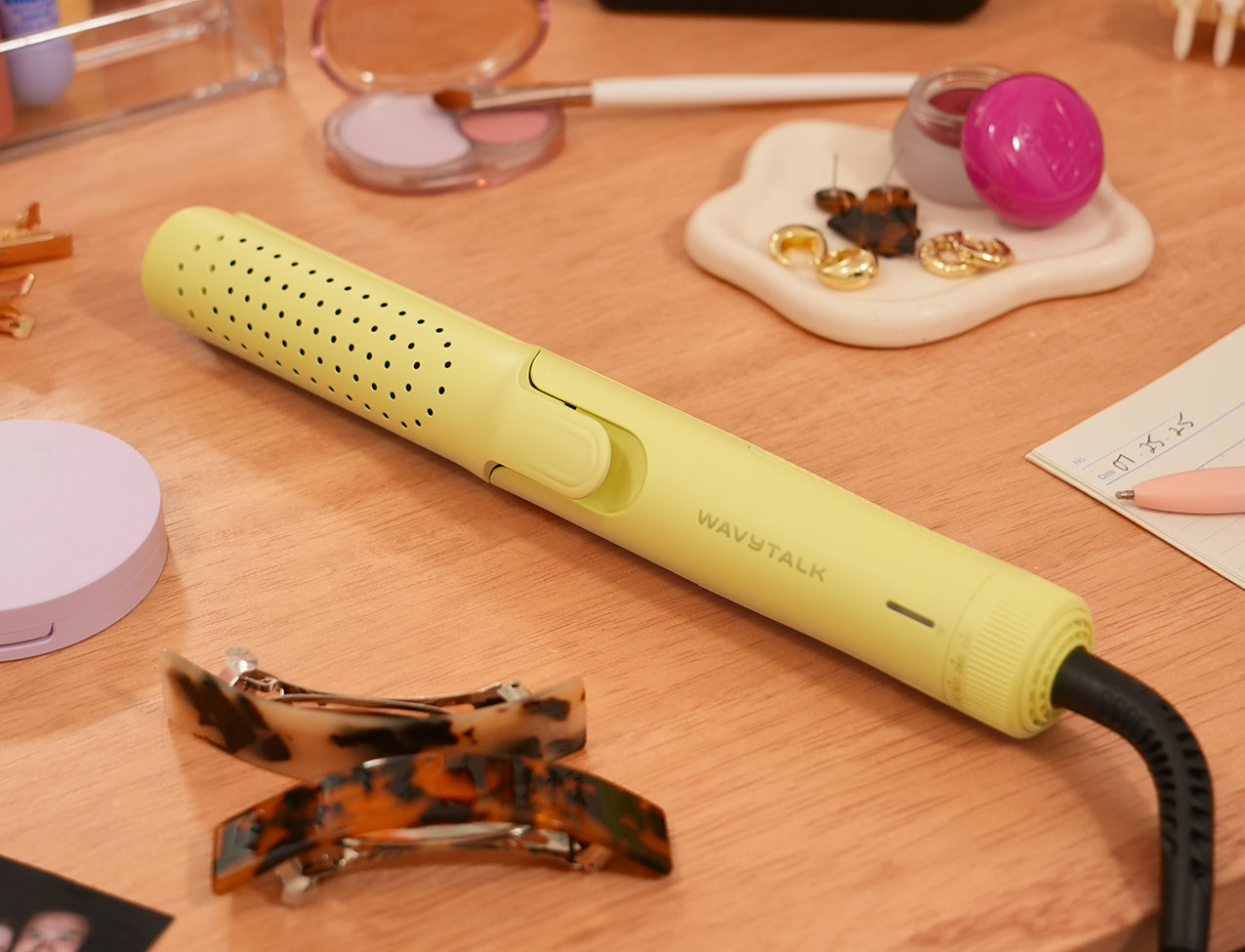 Yellow hair straightener on a wooden surface with hair clips and jewelry in the background