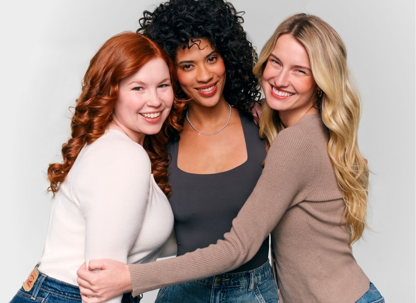 Three women with different hair colors posing together against a plain background
