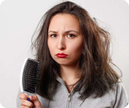 Woman holding a hairbrush with tangled hair against a plain background